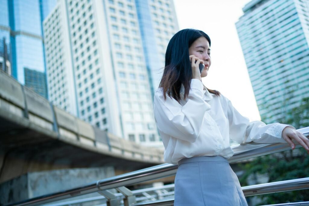 Mulher asiática confiante, vestida com traje de negócios, fala ao telefone na paisagem urbana de Bangkok.