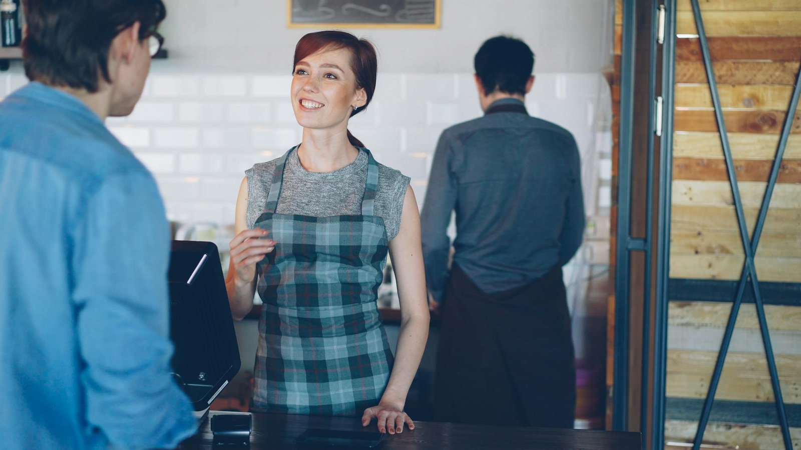 Barista sorridente no balcão, interagindo com um cliente em um café aconchegante.